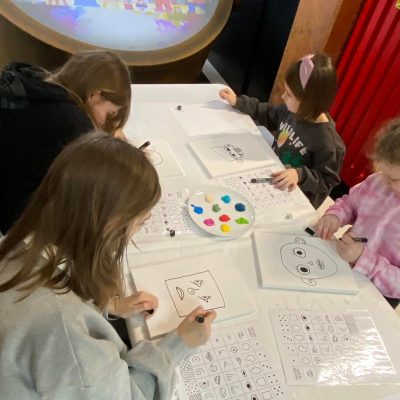 Czworo dzieci malujące obrazy inspirowane sztuką Pablo Picasso, w tle ekran w kształcie koła wyświetlający film o artyście